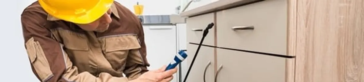 Roach exterminator applying treatment under kitchen cabinets in Norfolk, VA