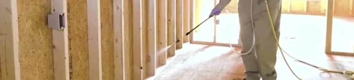Termite treatment technician applying spray along framing and unfinished walls in Norfolk, VA