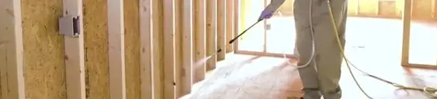 Termite treatment technician applying spray along framing and unfinished walls in Norfolk, VA